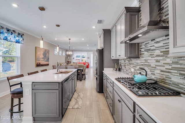 kitchen featuring wall chimney range hood, sink, gray cabinets, appliances with stainless steel finishes, and decorative light fixtures