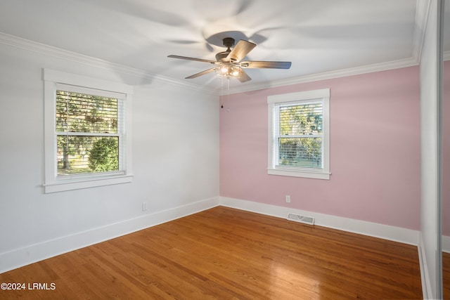 spare room featuring baseboards, visible vents, a ceiling fan, wood finished floors, and crown molding