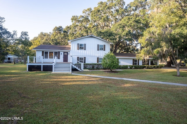 tri-level home featuring board and batten siding, a front yard, a deck, and stairs