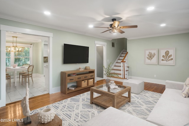 living area featuring stairs, crown molding, visible vents, wood finished floors, and ceiling fan with notable chandelier