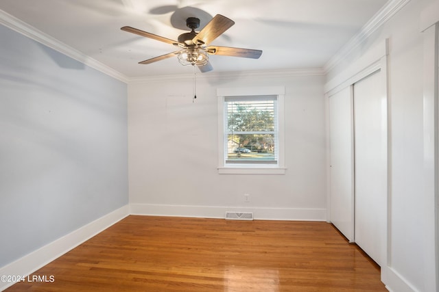 unfurnished bedroom featuring crown molding, a closet, visible vents, wood finished floors, and baseboards