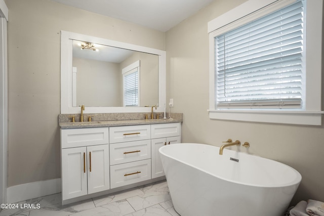 bathroom with double vanity, marble finish floor, a freestanding tub, and a sink