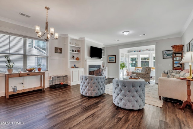 living room with crown molding, dark hardwood / wood-style flooring, a chandelier, and built in shelves