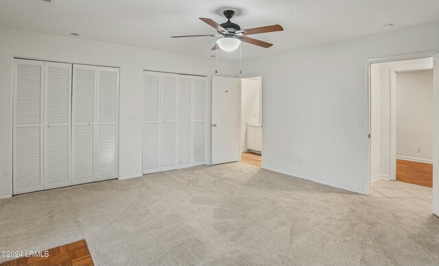 unfurnished bedroom with two closets, light colored carpet, and ceiling fan