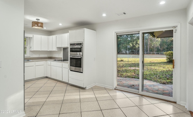 kitchen with black electric cooktop, stainless steel double oven, light tile patterned floors, and white cabinets