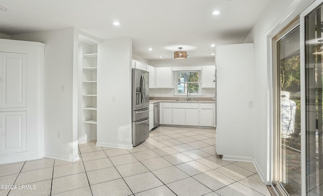 kitchen with built in shelves, sink, white cabinetry, light tile patterned floors, and appliances with stainless steel finishes