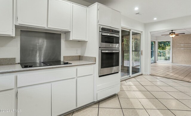 kitchen with light tile patterned flooring, ceiling fan, stainless steel double oven, black electric stovetop, and white cabinets