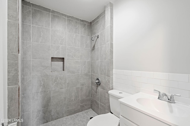 bathroom with vanity, toilet, tile walls, and a tile shower