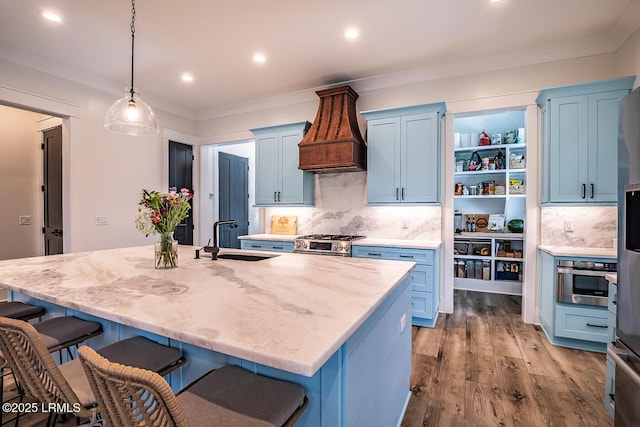 kitchen with stainless steel range, decorative light fixtures, an island with sink, and light hardwood / wood-style flooring