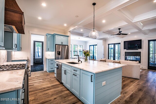 kitchen featuring light stone counters, appliances with stainless steel finishes, decorative light fixtures, and an island with sink