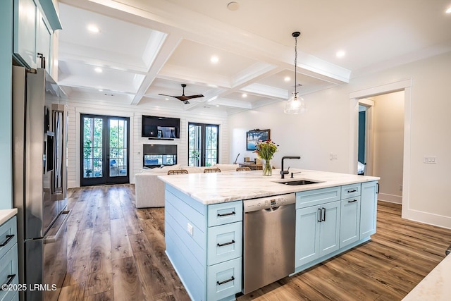 kitchen with sink, hanging light fixtures, a kitchen island with sink, stainless steel appliances, and light stone countertops