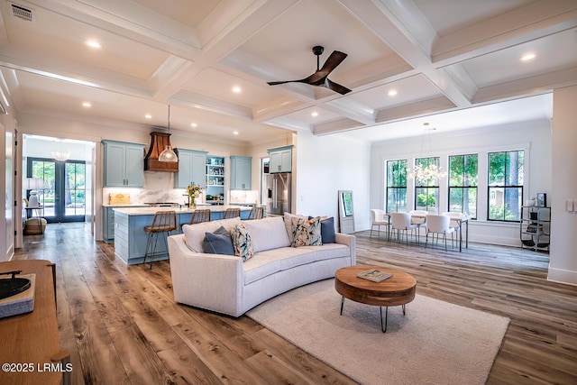 living room with coffered ceiling, ceiling fan with notable chandelier, beam ceiling, and light hardwood / wood-style flooring