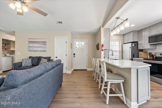 kitchen featuring sink, gray cabinetry, stainless steel appliances, a kitchen breakfast bar, and light wood-type flooring