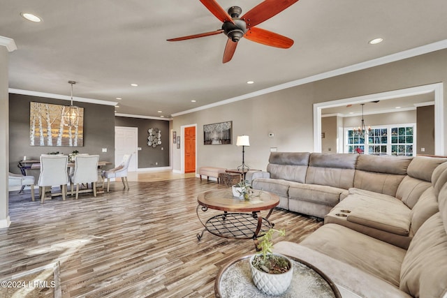 living room featuring hardwood / wood-style flooring, ceiling fan with notable chandelier, and ornamental molding