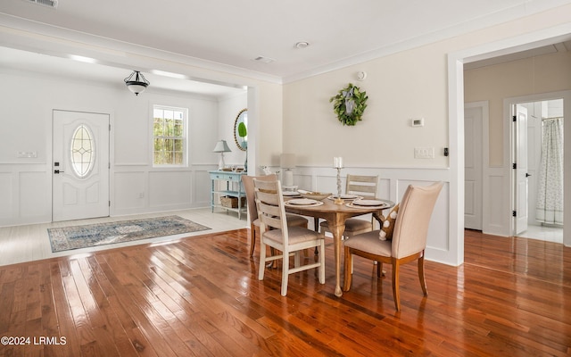 dining space featuring a decorative wall, wood finished floors, visible vents, and crown molding