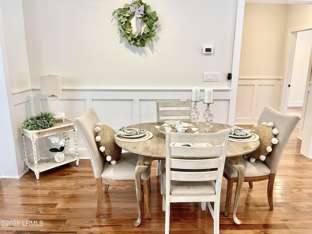 dining area featuring wainscoting, a decorative wall, and wood finished floors