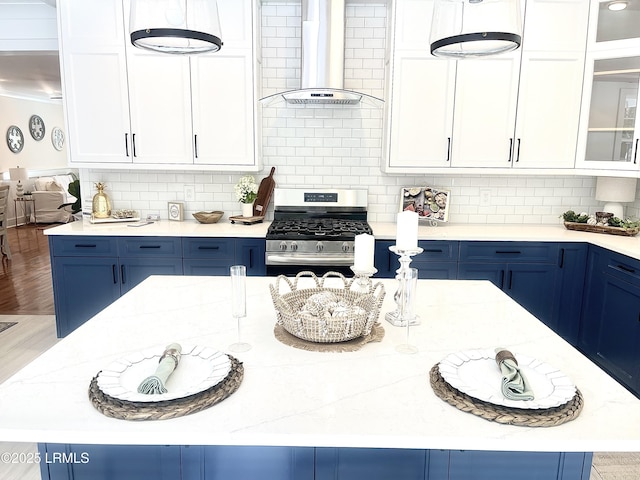 kitchen with stainless steel gas stove, wall chimney exhaust hood, blue cabinetry, and glass insert cabinets