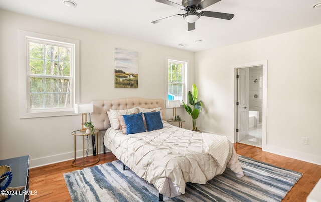 bedroom with ensuite bath, wood finished floors, visible vents, and baseboards