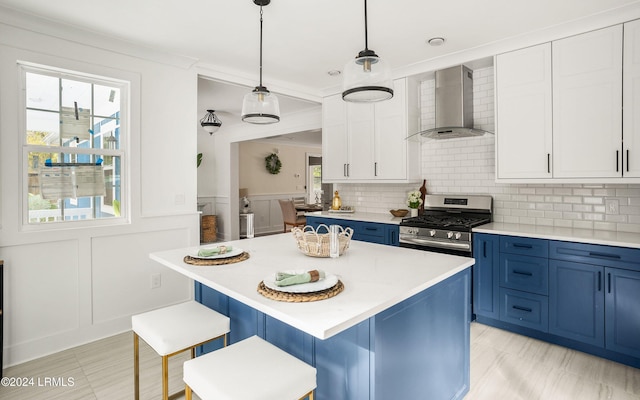 kitchen with blue cabinets, wall chimney range hood, stainless steel gas range, and light countertops