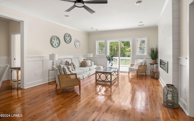 living area with ornamental molding, a tile fireplace, wainscoting, and wood finished floors