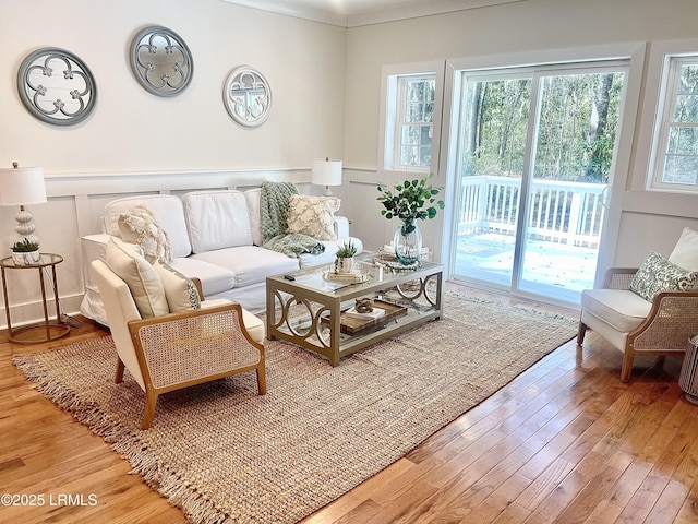 living area featuring crown molding, wainscoting, wood finished floors, and a decorative wall