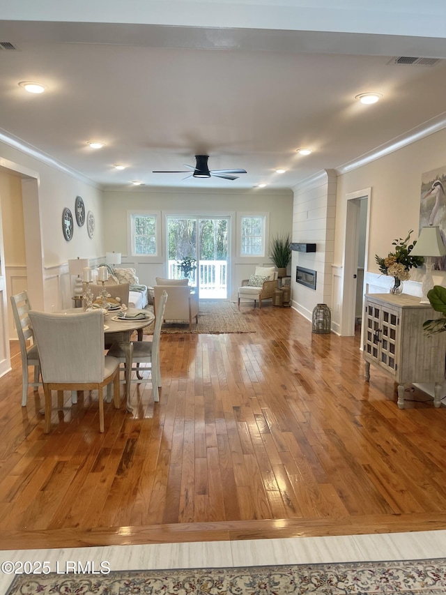 dining room featuring a large fireplace, visible vents, ornamental molding, and wood finished floors