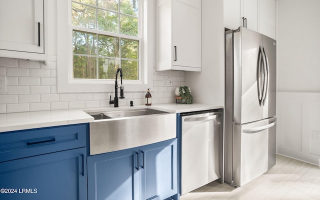 kitchen with white cabinets, stainless steel appliances, light countertops, blue cabinetry, and a sink