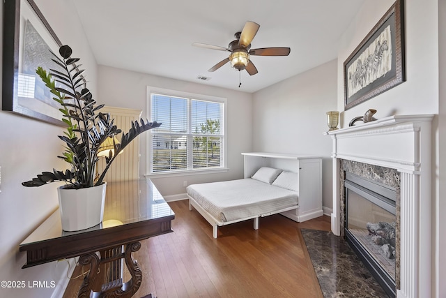 bedroom featuring a premium fireplace, ceiling fan, and dark hardwood / wood-style flooring