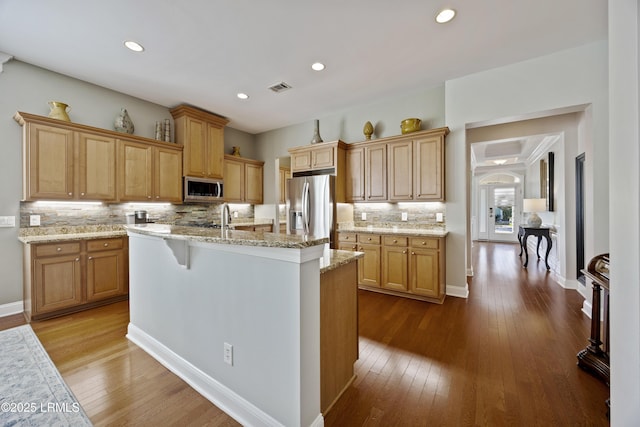 kitchen featuring hardwood / wood-style floors, appliances with stainless steel finishes, a breakfast bar area, and a center island with sink