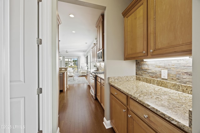 kitchen with light stone counters, appliances with stainless steel finishes, dark wood-type flooring, and decorative backsplash