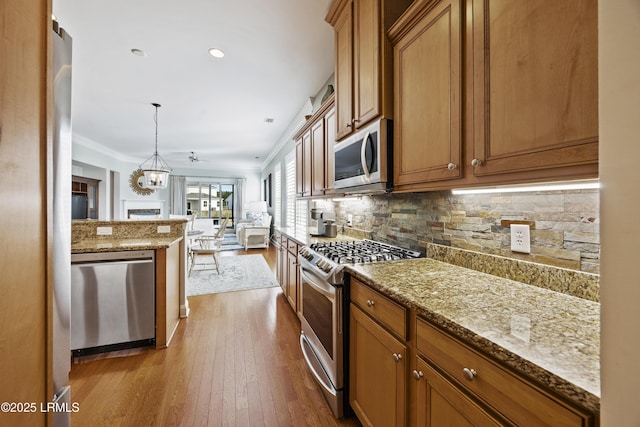 kitchen featuring appliances with stainless steel finishes, backsplash, light stone counters, and decorative light fixtures
