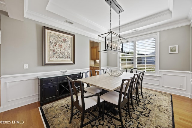 dining area featuring a chandelier, ornamental molding, a raised ceiling, and hardwood / wood-style floors