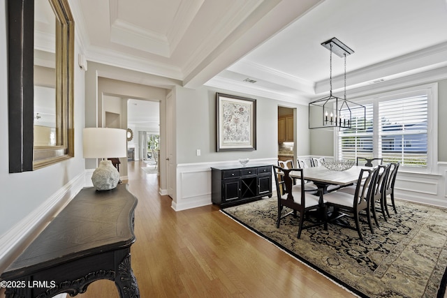 dining space with crown molding, a tray ceiling, an inviting chandelier, and light wood-type flooring