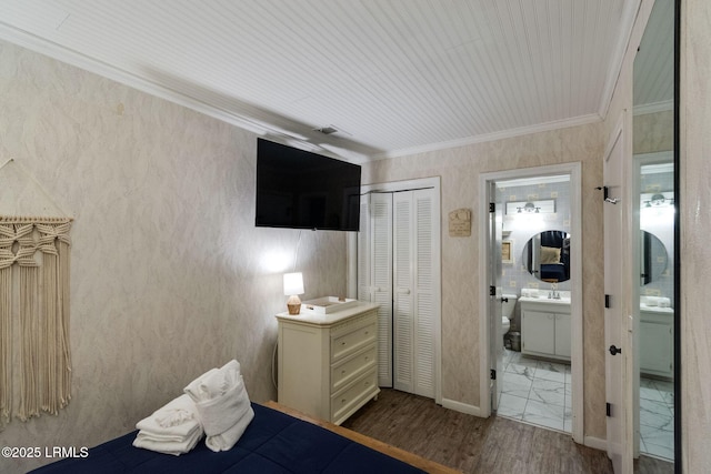 bedroom featuring a closet, ornamental molding, wood finished floors, ensuite bathroom, and a sink