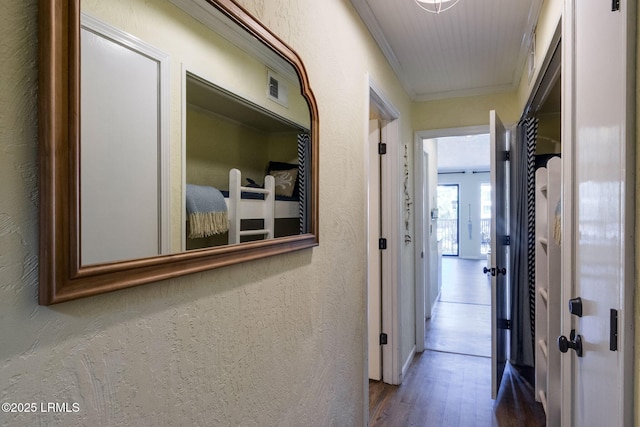 hallway featuring a textured wall, visible vents, crown molding, and wood finished floors