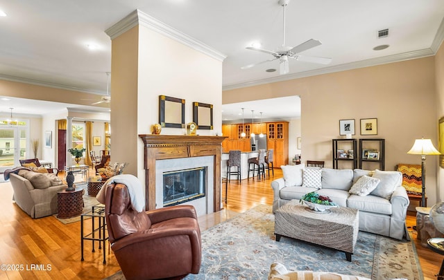 living room with ornamental molding, a high end fireplace, ceiling fan with notable chandelier, and light wood-type flooring