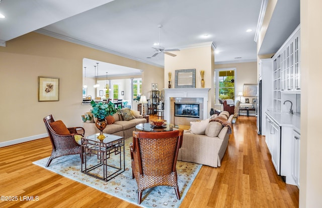 living room with ceiling fan, ornamental molding, a fireplace, and light hardwood / wood-style floors