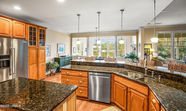 kitchen featuring dark stone counters, hanging light fixtures, stainless steel appliances, crown molding, and light wood-type flooring