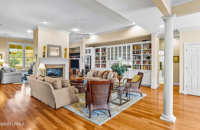 living room with decorative columns, a tiled fireplace, and light wood-type flooring