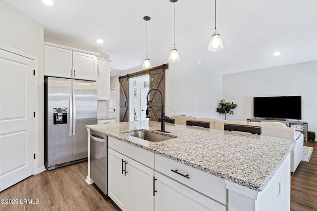 kitchen featuring sink, white cabinets, stainless steel appliances, a barn door, and a center island with sink