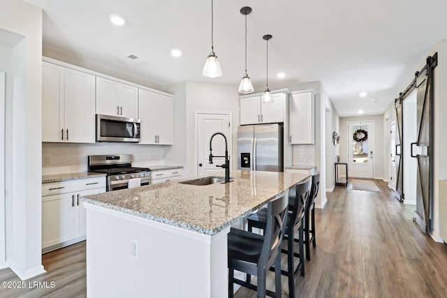 kitchen featuring sink, white cabinets, stainless steel appliances, a barn door, and a center island with sink