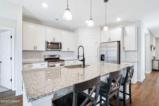 kitchen featuring sink, a kitchen island with sink, hanging light fixtures, stainless steel appliances, and white cabinets