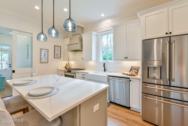 kitchen featuring premium range hood, high quality appliances, hanging light fixtures, and white cabinets