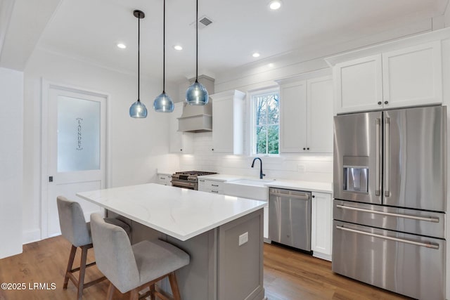 kitchen featuring a kitchen island, high quality appliances, white cabinets, backsplash, and hanging light fixtures