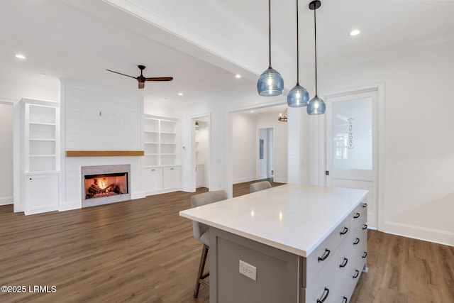 kitchen featuring a center island, dark hardwood / wood-style floors, pendant lighting, ceiling fan, and a fireplace