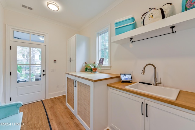 interior space with ornamental molding, sink, white cabinets, and light wood-type flooring