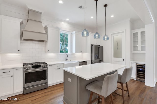 kitchen with sink, white cabinetry, stainless steel appliances, a center island, and beverage cooler