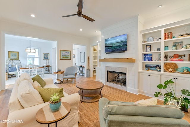 living room with built in shelves, light hardwood / wood-style flooring, ornamental molding, ceiling fan, and a fireplace