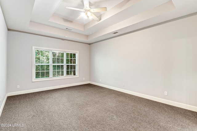 carpeted empty room featuring ceiling fan and a raised ceiling