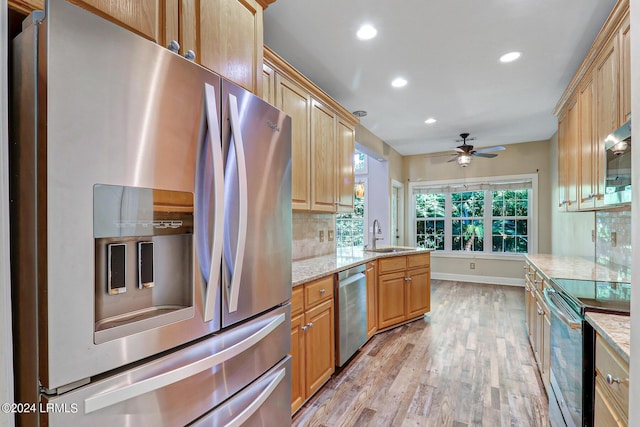 kitchen with light stone countertops, appliances with stainless steel finishes, sink, and light wood-type flooring